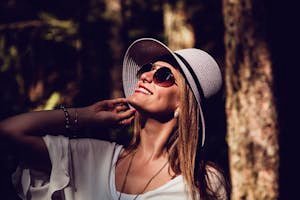 A fashionable woman in sunglasses and hat enjoying a sunny day outdoors, radiating confidence and joy.