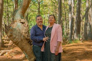 A joyful couple standing together in a sunlit forest, enjoying a summer day.
