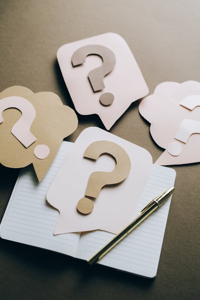 Artistic paper question marks on an open notebook with a pen, symbolizing questions needed to be answered